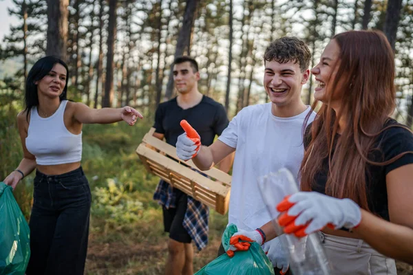 ティーンエイジャーの友人のグループ 男性と女性の慎重な男性 ゴミ捨てプラスチックボトルと森から紙を拾う女性 晴れた日の環境ケアのエコロジーの概念で自然をきれいにする — ストック写真