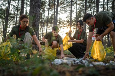 Bir grup genç arkadaş Z erkek ve beyaz kadın atık plastik şişeleri ve kağıtları toplayarak güneşli bir günde çevre koruma kavramının doğasını temizliyorlar.