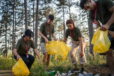 Bir grup genç arkadaş Z erkek ve beyaz kadın atık plastik şişeleri ve kağıtları toplayarak güneşli bir günde çevre koruma kavramının doğasını temizliyorlar.