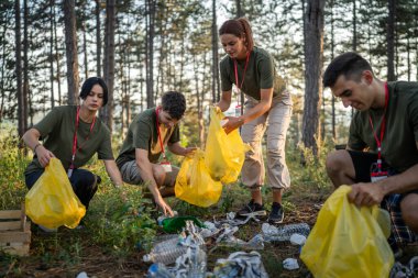 Bir grup genç arkadaş Z erkek ve beyaz kadın atık plastik şişeleri ve kağıtları toplayarak güneşli bir günde çevre koruma kavramının doğasını temizliyorlar.