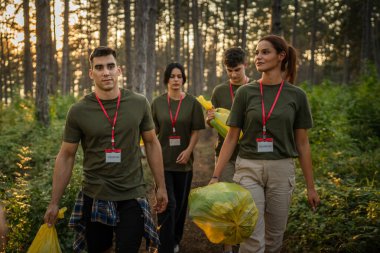 Bir grup genç arkadaş Z erkek ve beyaz kadın atık plastik şişeleri ve kağıtları toplayarak güneşli bir günde çevre koruma kavramının doğasını temizliyorlar.