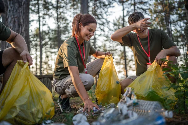 group of teenage friends gen Z male and female caucasian men women picking up waste garbage plastic bottles and paper from the forest cleaning up nature in sunny day environmental care ecology concept