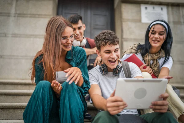 一群高加索青少年朋友坐在学校或大学前 举行数字平板电脑观看视频电影 或通过视频上网浏览社交网络真实的人 — 图库照片
