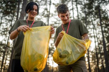 Çift ya da genç arkadaşlar Z erkek ve beyaz kadın atık plastik şişeleri ve kağıtları toplayarak güneşli bir günde çevre koruma kavramının doğasını temizlerler.