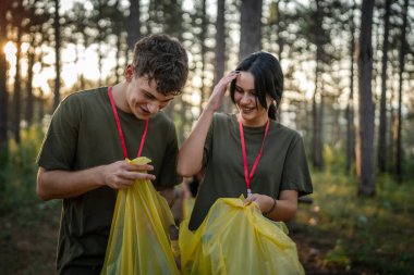Çift ya da genç arkadaşlar Z erkek ve beyaz kadın atık plastik şişeleri ve kağıtları toplayarak güneşli bir günde çevre koruma kavramının doğasını temizlerler.
