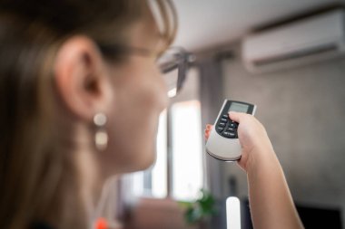 Bir beyaz kadın televizyon veya klima için uzaktan kumanda kullanıyor.