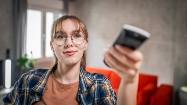 Bir beyaz kadın televizyon veya klima için uzaktan kumanda kullanıyor.