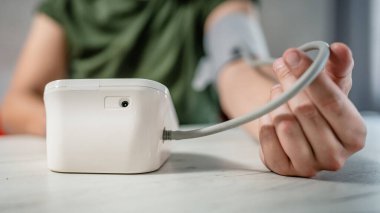 Beyaz bir erkek masada oturuyor. Kan basıncını ölçmek için evde gerçek sağlık hizmetleri konseptini kullanıyor.