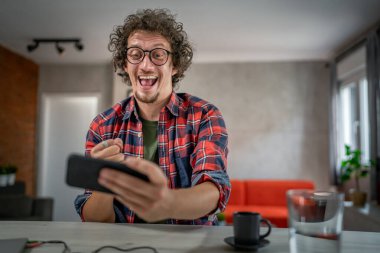 Beyaz adam evinde oturup akıllı cep telefonuyla video oyunları oynuyor.