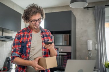 Beyaz bir adam online alışveriş ürünlerinin nakliye detaylarını kontrol etmek için akıllı telefon kullanıyor. Akıllı telefon uygulaması başvurusunu kontrol edin. Çevrimiçi detaylar mutlu bir gülümseme.