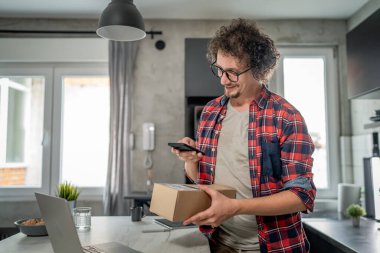 Beyaz bir adam online alışveriş ürünlerinin nakliye detaylarını kontrol etmek için akıllı telefon kullanıyor. Akıllı telefon uygulaması başvurusunu kontrol edin. Çevrimiçi detaylar mutlu bir gülümseme.