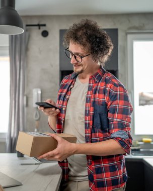Beyaz bir adam online alışveriş ürünlerinin nakliye detaylarını kontrol etmek için akıllı telefon kullanıyor. Akıllı telefon uygulaması başvurusunu kontrol edin. Çevrimiçi detaylar mutlu bir gülümseme.