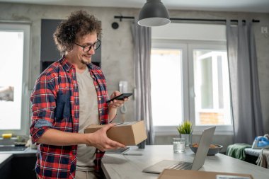 Beyaz bir adam online alışveriş ürünlerinin nakliye detaylarını kontrol etmek için akıllı telefon kullanıyor. Akıllı telefon uygulaması başvurusunu kontrol edin. Çevrimiçi detaylar mutlu bir gülümseme.