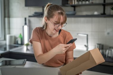 Beyaz bir kadın, online alışveriş ürünlerinin nakliye detaylarını kontrol etmek için akıllı telefon kullanıyor. Akıllı telefon uygulaması başvurusunu kontrol edin. Çevrimiçi detaylar mutlu bir gülümseme.