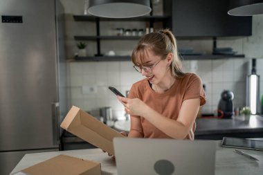 Beyaz bir kadın, online alışveriş ürünlerinin nakliye detaylarını kontrol etmek için akıllı telefon kullanıyor. Akıllı telefon uygulaması başvurusunu kontrol edin. Çevrimiçi detaylar mutlu bir gülümseme.
