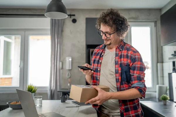 Beyaz bir adam online alışveriş ürünlerinin nakliye detaylarını kontrol etmek için akıllı telefon kullanıyor. Akıllı telefon uygulaması başvurusunu kontrol edin. Çevrimiçi detaylar mutlu bir gülümseme.