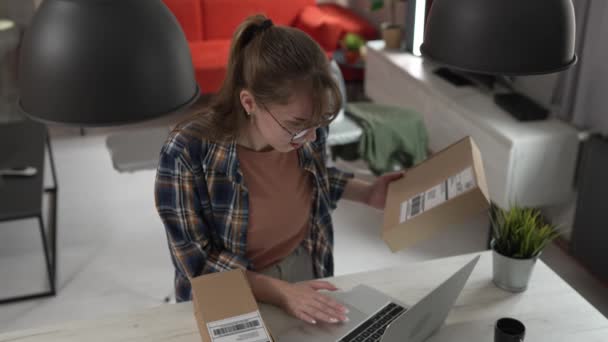 1人の白人女性は受け取られたパッケージの船積みの細部を点検するためにラップトップのコンピュータを使用します オンラインショッピング プロダクト着きました スタンド アプリケーション チェック オンライン細部 — ストック動画