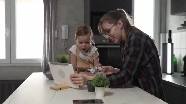 小高加索女孩蹒跚学步和她的妈妈或阿姨在家里的厨房里玩手指木偶 在数字化平板电脑前玩着有趣的休闲结合概念慢动作 — 图库视频影像
