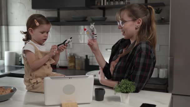 小高加索女孩蹒跚学步和她的妈妈或阿姨在家里的厨房里玩手指木偶 在数字化平板电脑前玩着有趣的休闲结合概念慢动作 — 图库视频影像