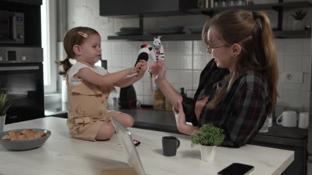小さな白人少女トッドラーと彼女の母親や叔母は楽しいレジャーボンディングコンセプトのスローモーションを持つデジタルタブレットの前にキッチンで自宅で指の人形で遊ぶ — ストック動画