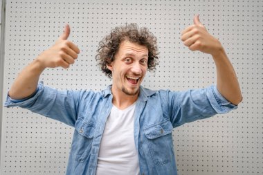 Kafkasyalı yetişkin bir adamın portresi açık havada duruyor mavi gömlekli mutlu bir gülümseme takınıyor kendinden emin fotokopi odası önünde dururken duvar belini yukarı kaldırması olumlu duygu kavramını olumlu yönde etkiliyor.