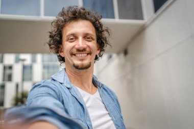 Kafkasyalı yetişkin bir adamın portresi açık havada duruyor mavi gömlek giyiyor mutlu bir gülümseme takınıyor kendine güvenen bir kopya alanı.