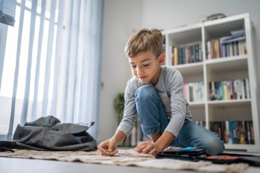 Küçük beyaz çocuk sırt çantasını okula dönüş ve eğitim konseptine hazırla. Evde oturup eşyalarını topla. Gerçek insanlar yer kopyalayabilir.