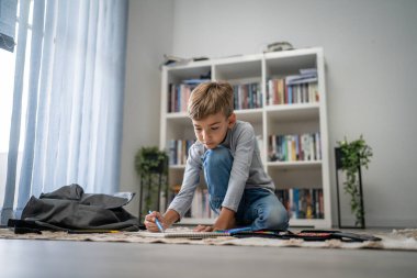 Bir okul çocuğu. Küçük beyaz bir çocuk evde oynuyor. Ev ödevlerini yapıyor. Çocukluk gelişimi ve eğitim kavramı.