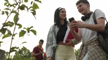 Okulun önündeki birkaç beyaz genç öğrenci cep telefonu kullanıyor. Akıllı telefon, erkek ve kadın arkadaşlar, kampüsün önündeki beyaz erkek ve kadın gençler okul konseptine geri dönüyorlar.