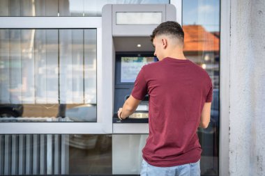 Genç bir erkek öğrenci kredi kartı kullanıyor ve ATM 'den para çekiyor.