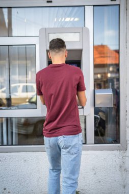 Genç bir erkek öğrenci kredi kartı kullanıyor ve ATM 'den para çekiyor.