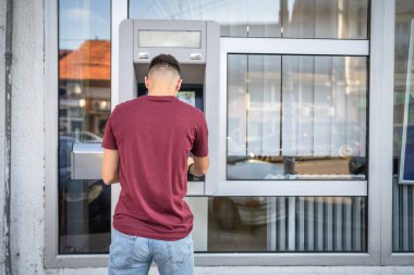 Genç bir erkek öğrenci kredi kartı kullanıyor ve ATM 'den para çekiyor.