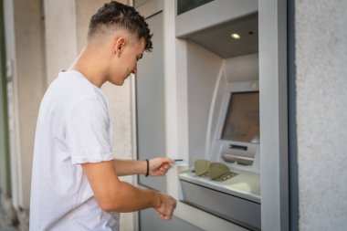 Genç bir erkek öğrenci kredi kartı kullanıyor ve ATM 'den para çekiyor.