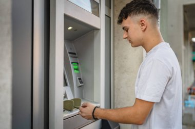 Genç bir erkek öğrenci kredi kartı kullanıyor ve ATM 'den para çekiyor.