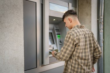 Genç bir erkek öğrenci kredi kartı kullanıyor ve ATM 'den para çekiyor.