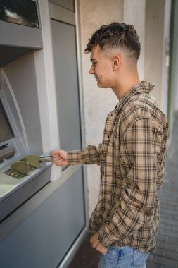 Genç bir erkek öğrenci kredi kartı kullanıyor ve ATM 'den para çekiyor.