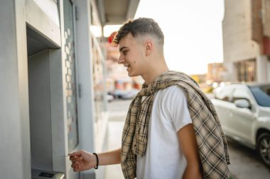Genç bir erkek öğrenci kredi kartı kullanıyor ve ATM 'den para çekiyor.