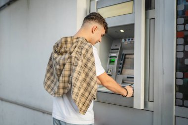 Genç bir erkek öğrenci kredi kartı kullanıyor ve ATM 'den para çekiyor.