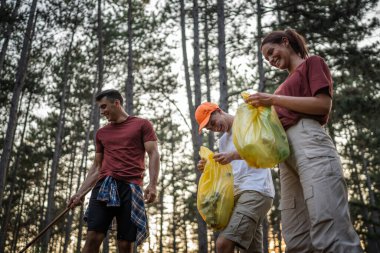 Bir grup genç arkadaş Z erkek ve beyaz kadın atık plastik şişeleri ve kağıtları toplayarak güneşli bir günde çevre koruma kavramının doğasını temizliyorlar.