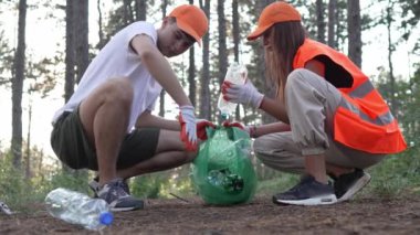 Bir grup genç arkadaş Z erkek ve beyaz kadın atık plastik şişeleri ve kağıtları toplayarak güneşli bir günde çevre koruma kavramının doğasını temizliyorlar.