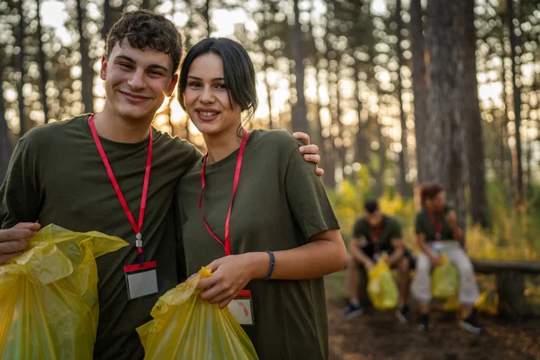 友人のグループの前の肖像カップル ボランティアは夏の日の遅い動きでゴミやきれいな森の性質を収集する準備 — ストック写真