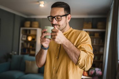 Kafkasyalı genç bir adam, sabahları evde gömlek giyerken kahve içiyor. Gerçek insanlar uzayı taklit ediyor.