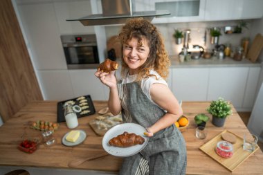 Yetişkin bir Kafkasyalı kadın her sabah kahvaltıda taze kruvasanla mutfakta duruyor.