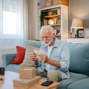 Bir son sınıf büyükbaba emeklisi gri saçlı ve sakallı hediye alıyor açık kutuda kart okuyarak mutlu bir gülümseme evde dizüstü bilgisayarın önünde internetten fotokopi odası arıyor.