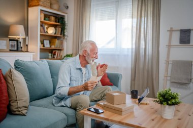 Bir son sınıf büyükbaba emeklisi gri saçlı ve sakallı hediye alıyor açık kutuda kart okuyarak mutlu bir gülümseme evde dizüstü bilgisayarın önünde internetten fotokopi odası arıyor.