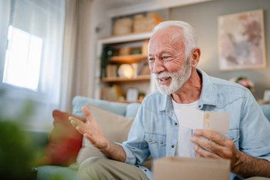 Bir son sınıf büyükbaba emeklisi gri saçlı ve sakallı hediye alıyor açık kutuda kart okuyarak mutlu bir gülümseme evde dizüstü bilgisayarın önünde internetten fotokopi odası arıyor.