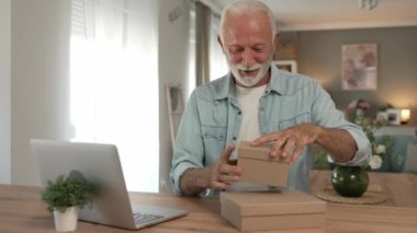 Bir son sınıf büyükbaba emeklisi gri saçlı ve sakallı hediye alıyor açık kutuda kart okuyarak mutlu bir gülümseme evde dizüstü bilgisayarın önünde internetten fotokopi odası arıyor.