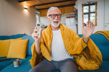 Beyaz tenli son sınıf öğrencisi bir adam evdeki kanepede oturur termometreyi tutar vücut ısısını kontrol eder ya da soğuk algınlığına yakalanır.