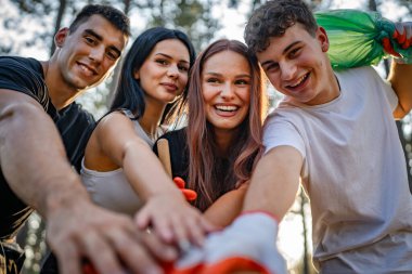 Bir grup genç arkadaş Z erkek ve beyaz kadın atık plastik şişeleri ve kağıtları toplayarak güneşli bir günde çevre koruma kavramının doğasını temizliyorlar.