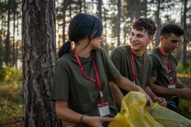 Bir grup genç arkadaş Z erkek ve beyaz kadın atık plastik şişeleri ve kağıtları toplayarak güneşli bir günde çevre koruma kavramının doğasını temizliyorlar.